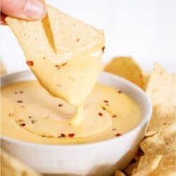 Quick Nacho Cheese Sauce in a bowl with a tortilla chip being dipped into the sauce.