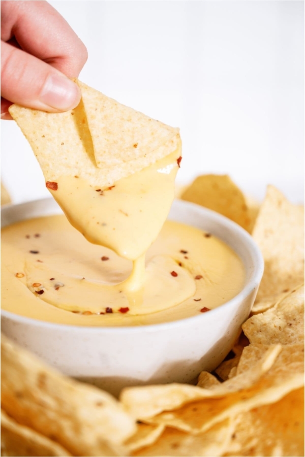 Quick Nacho Cheese Sauce in a bowl with a tortilla chip being dipped into the sauce.