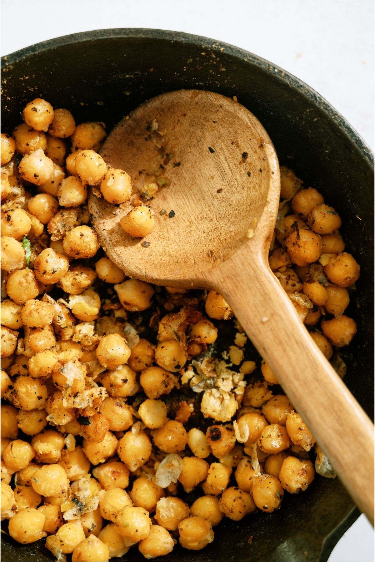 Chickpeas in a skillet with a wooden spoon.