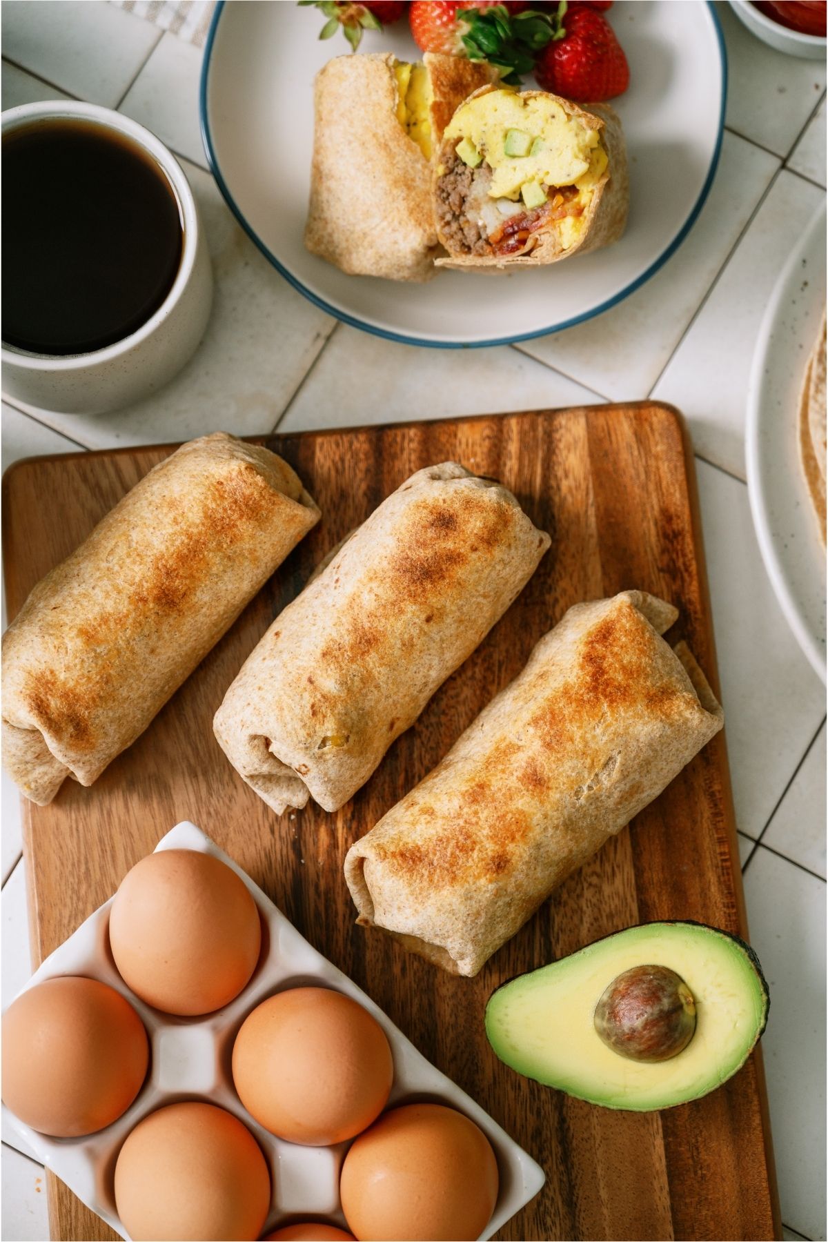 Top view of Loaded Breakfast Burritos on a cutting board surrounded by sliced avocados.