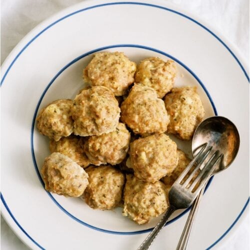 A white bowl of Cheesy Chicken Meatballs with a fork and spoon.
