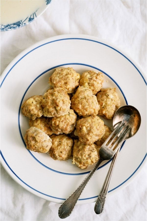 A white bowl of Cheesy Chicken Meatballs with a fork and spoon.