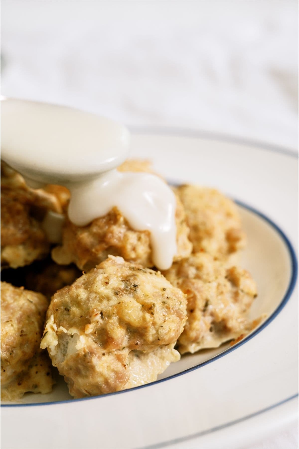 Spooning alfredo sauce on top of Cheesy Chicken Meatballs.