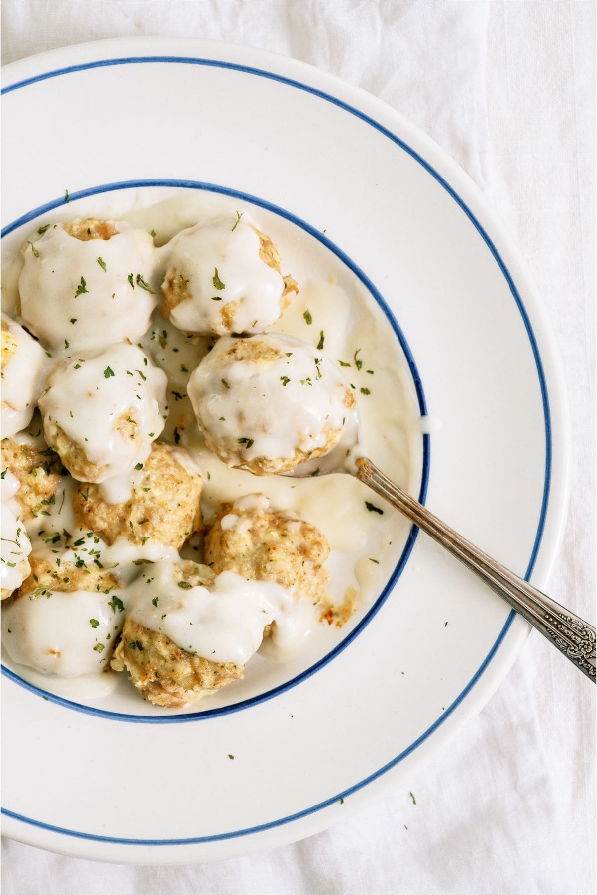 A bowl of Cheesy Chicken Meatballs topped with alfredo sauce.
