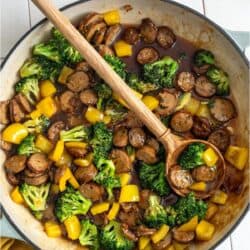 A pan of Chicken And Sausage Stir Fry with a wooden spoon.