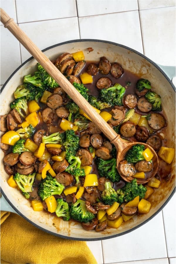 A pan of Chicken And Sausage Stir Fry with a wooden spoon.