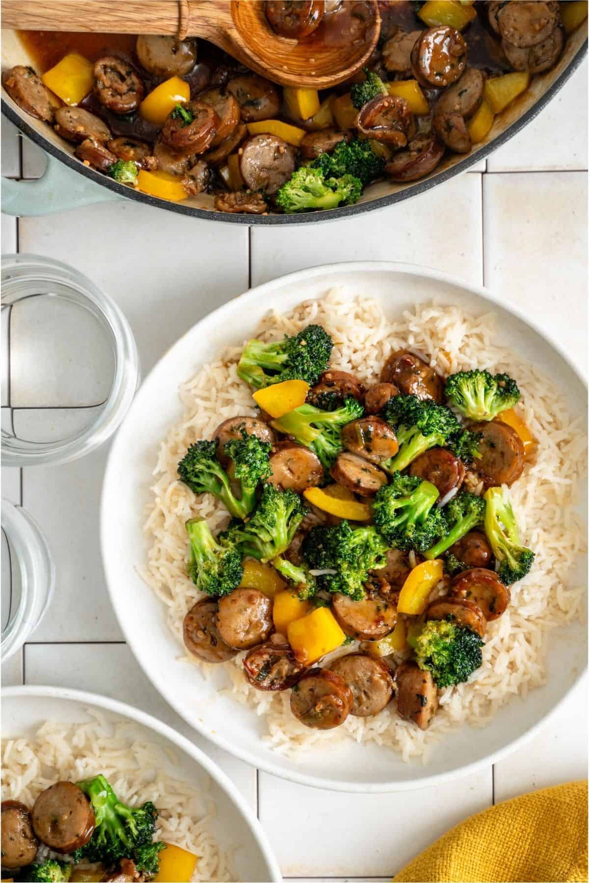 A serving of Chicken And Sausage Stir Fry on a plate of rice. The remaining Chicken And Sausage Stir Fry in the background.