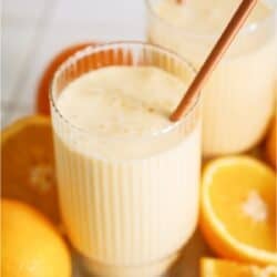 Orange julius smoothie in a cup surrounded with a straw and oranges.