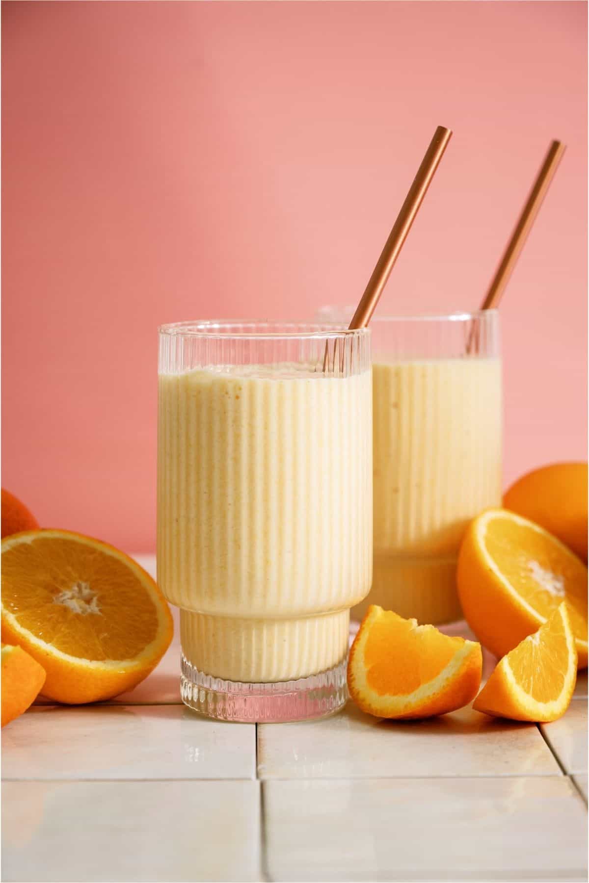 2 cups of Copycat Orange Julius with straws, surrounded by oranges.