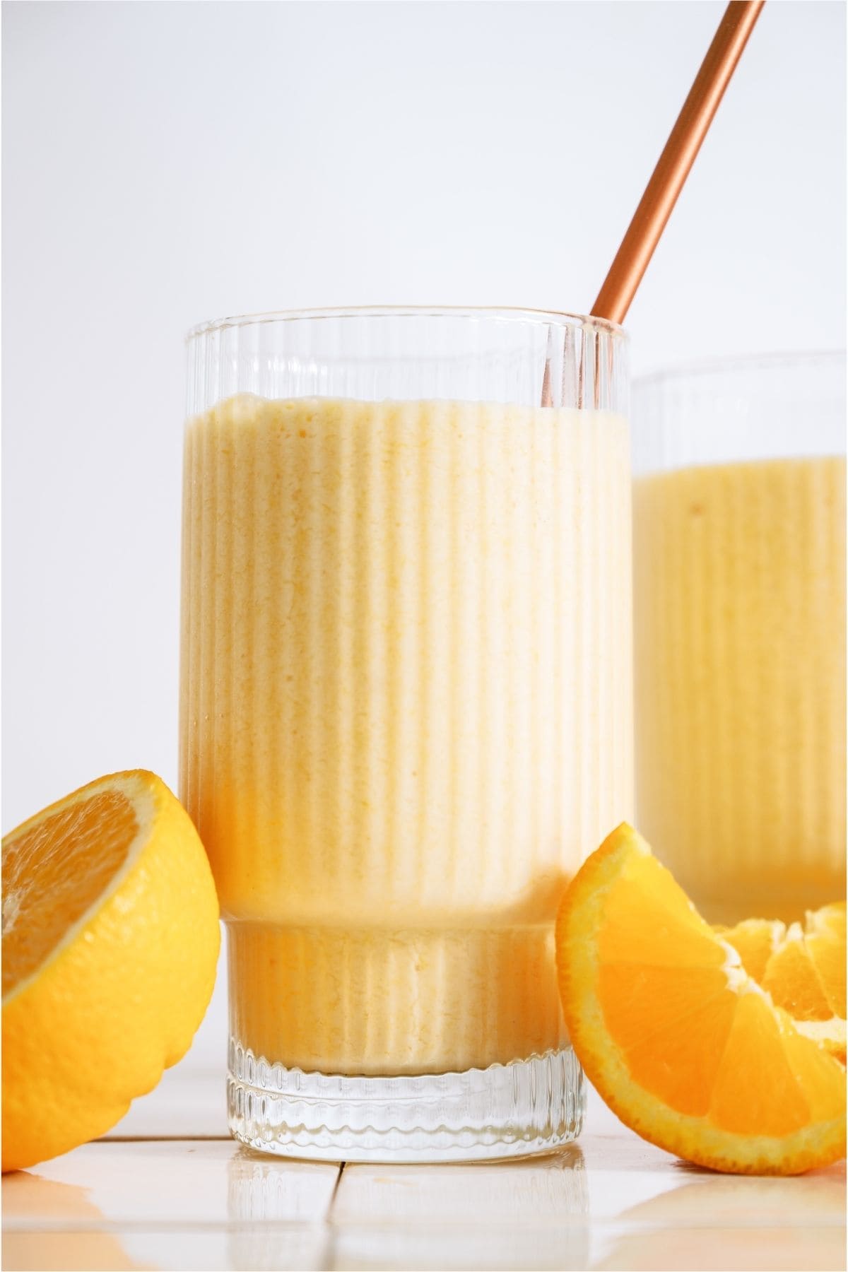 2 glasses of Copycat Orange Julius, the one in fronts with a straw. Sliced oranges around the glasses.