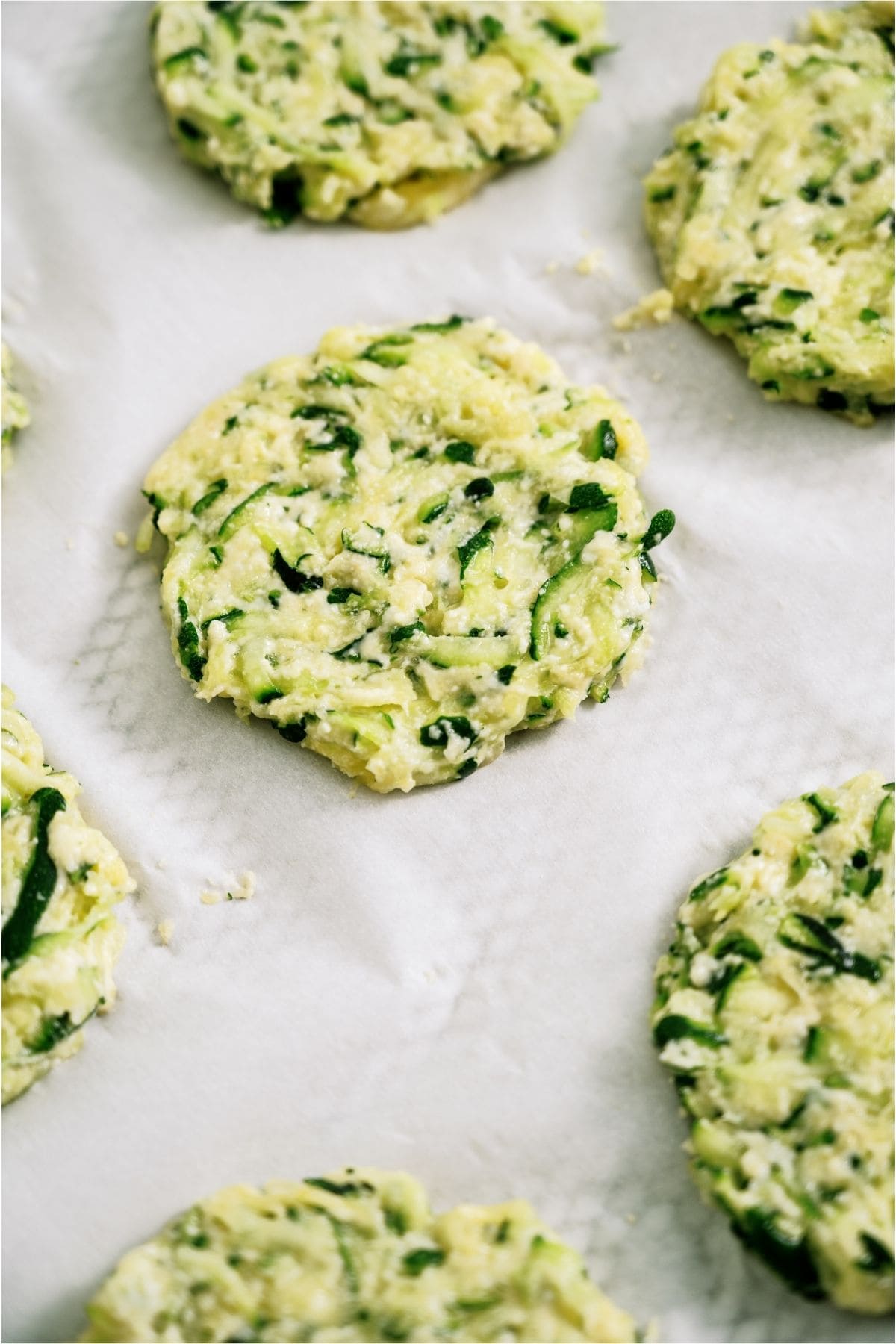 Uncooked Zucchini Fritters on parchment paper.