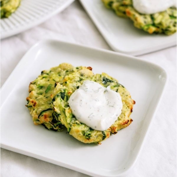 Crispy Air Fryer Zucchini Fritters on a plate topped with dill sour cream dip.