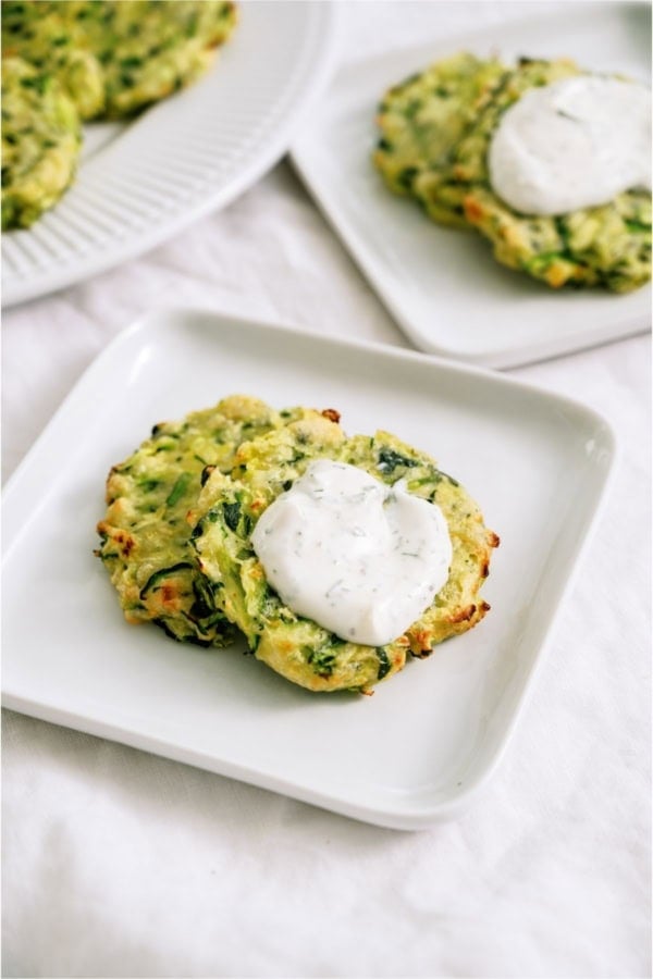 Crispy Air Fryer Zucchini Fritters on a plate topped with dill sour cream dip.