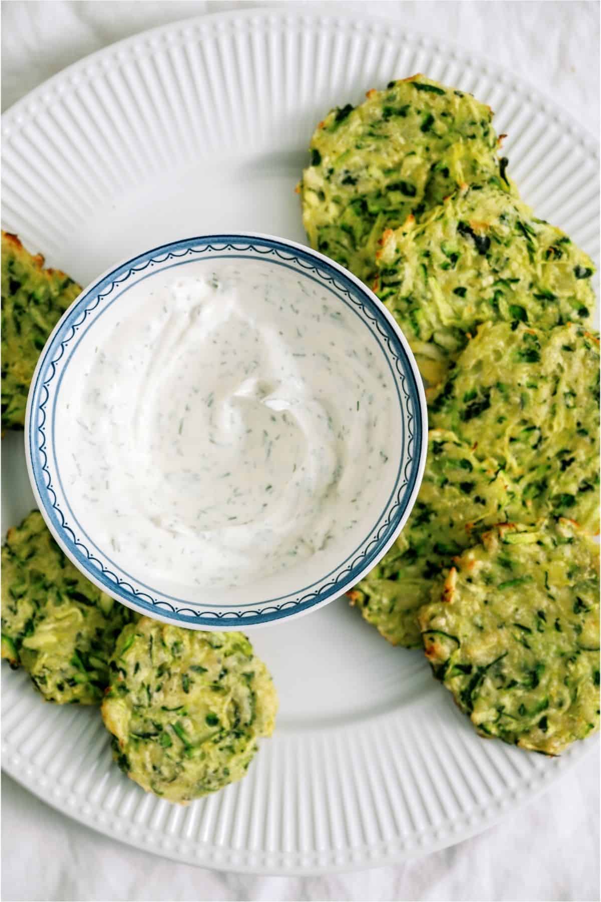 Crispy Zucchini Fritters surrounding a bowl of sour cream / dill sauce.