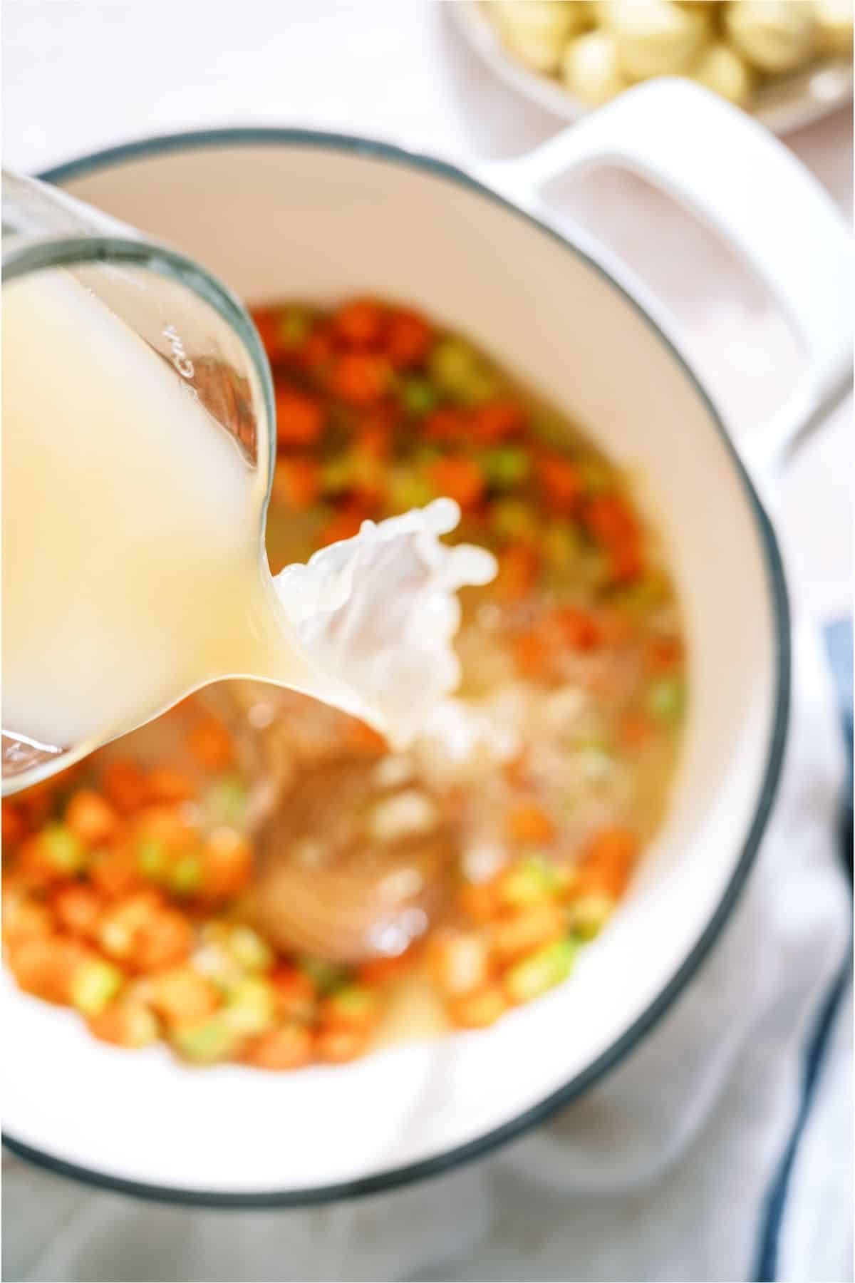 Pouring chicken broth into a stock pot filled with veggies.