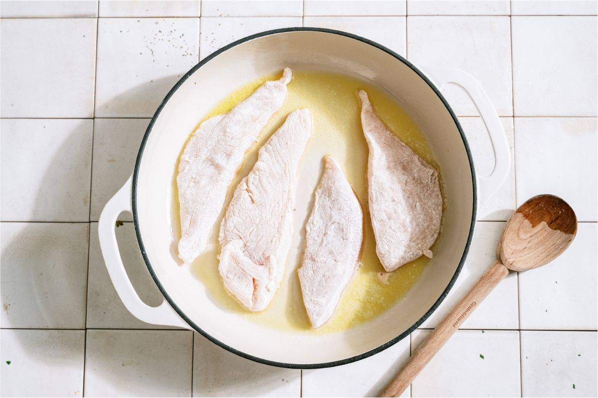 Floured chicken sections in a large skillet.