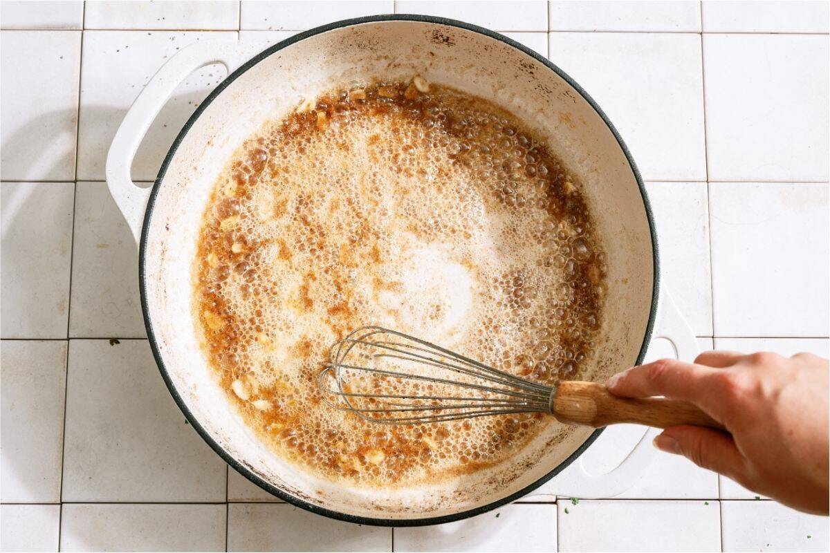 Whisking brown bits and sauce in a skillet.
