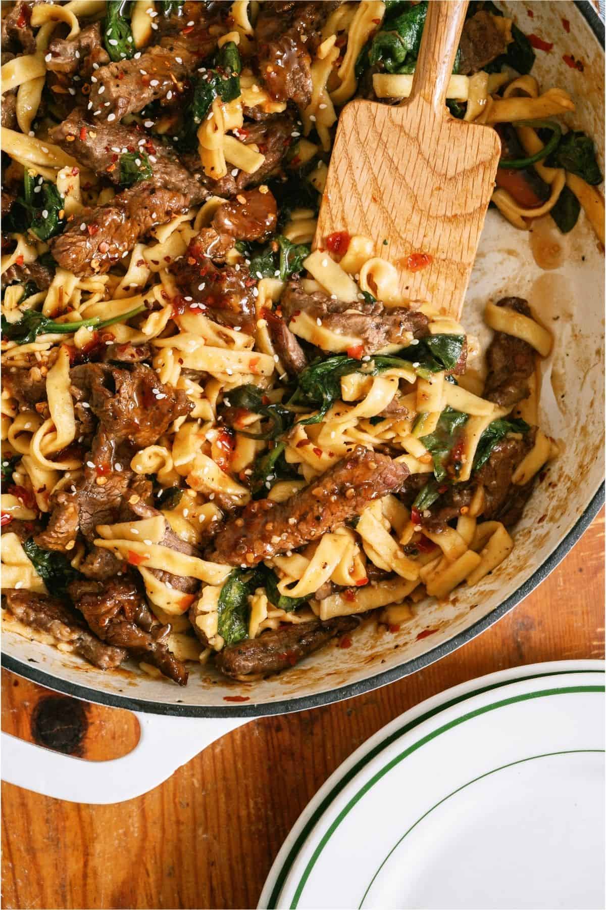 A pan of Beef and Noodles with a wooden spatula.