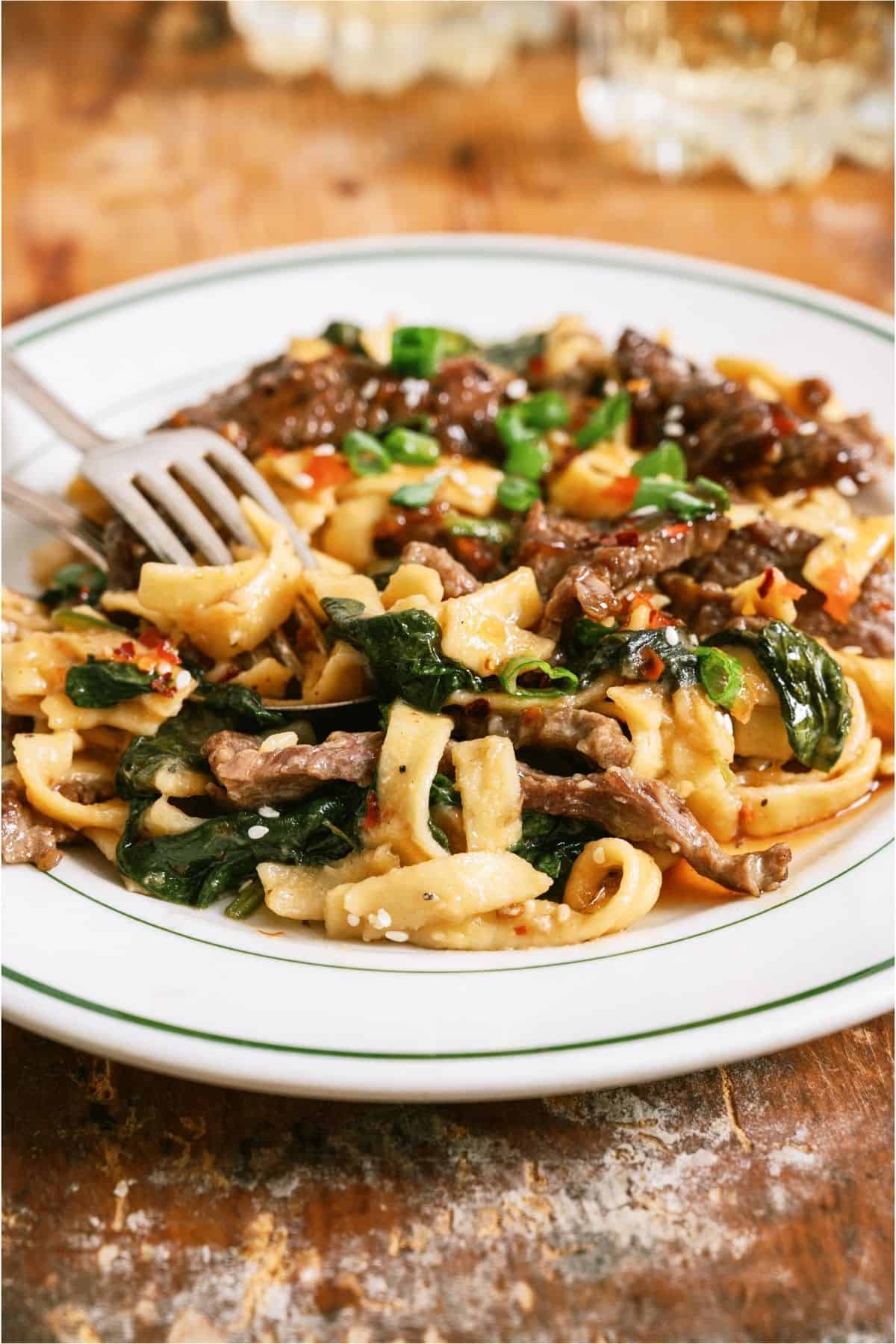 A white bowl with Beef and Noodles in it and a fork.