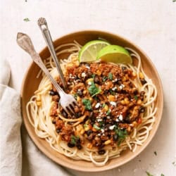 A bowl of Taco Spaghetti with 2 forks and garnished with sliced limes.