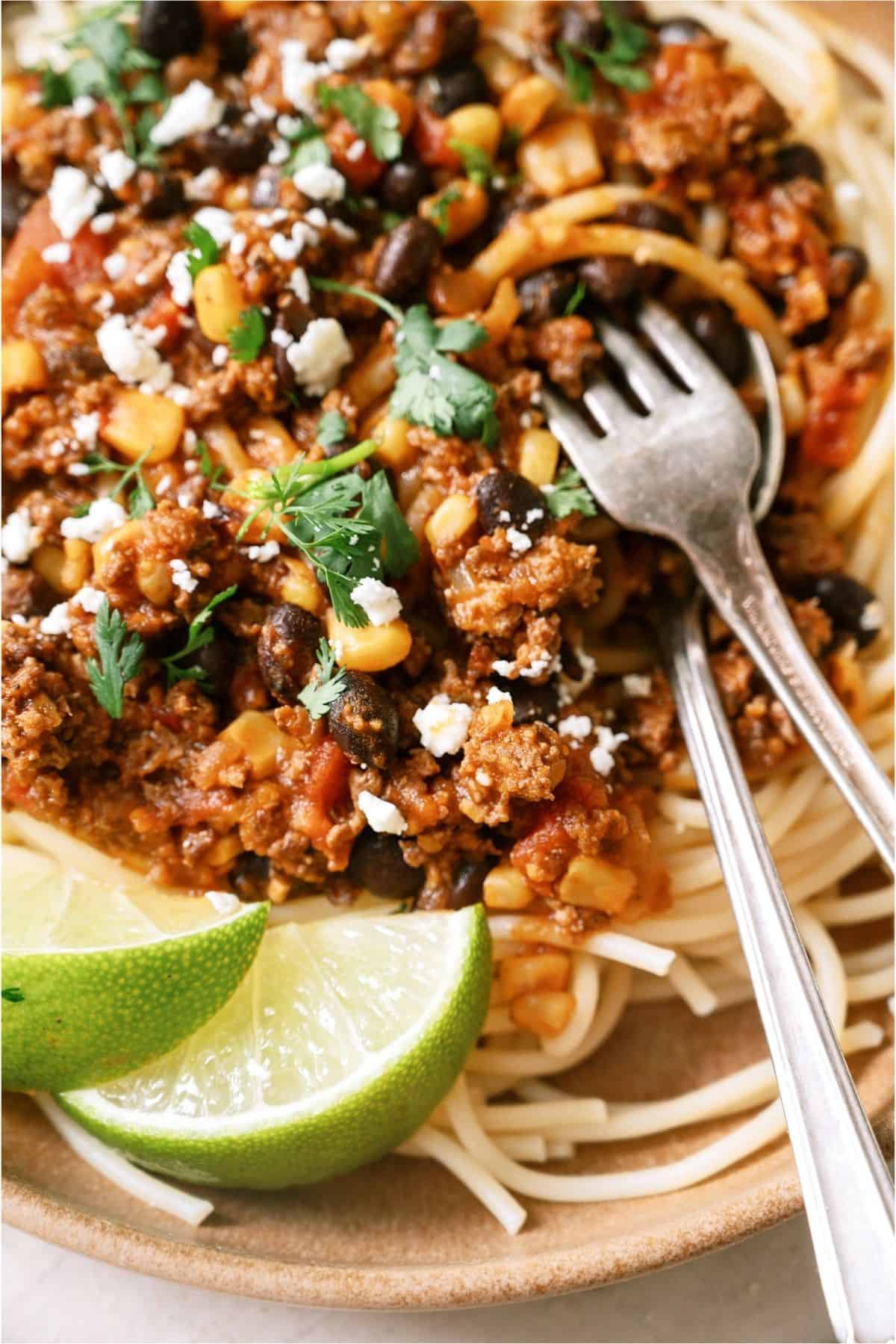 Close up of Taco Spaghetti with 2 forks and garnished with sliced limes.