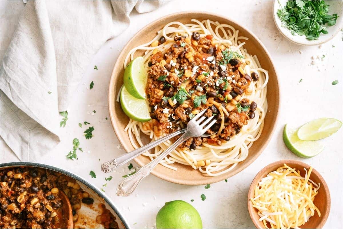 A bowl of Taco Spaghetti with two forks and a small bowl of cheese on the side.