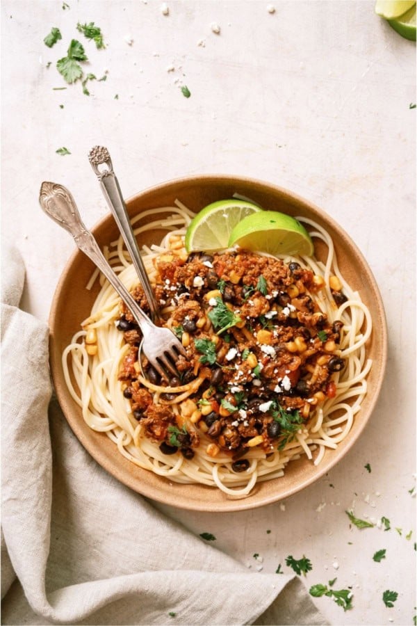 A bowl of Taco Spaghetti with 2 forks and garnished with sliced limes.