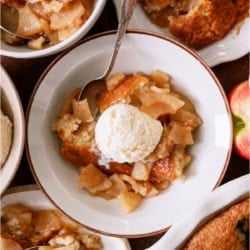 A bowl with a serving of Easy Apple Cobbler topped with a scoop of ice cream. Other bowls of Easy Apple Cobbler surrounding it.