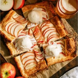 An apple tart cut into 6 squares some topped with a scoop of ice cream. Fresh apples on the side.