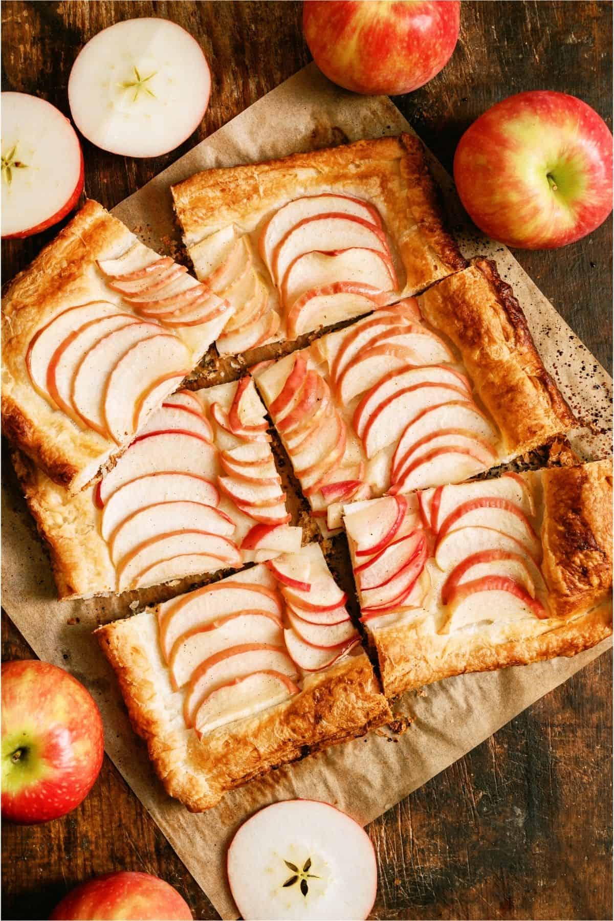 Apple Tart cut into 6 squares with fresh apples surround the tart.