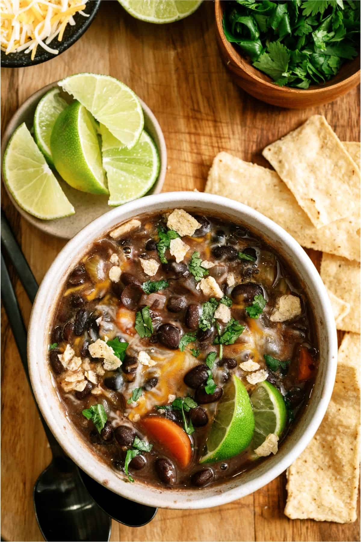 A bowl of Easy Black Bean Soup with limes, tortilla chips and cilantro in the background.