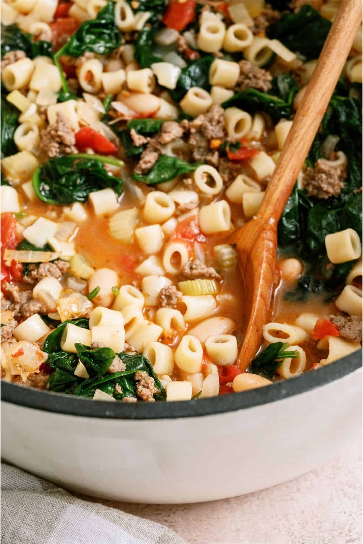 A wooden spoon stirring a large post of Pasta Fagioli soup.