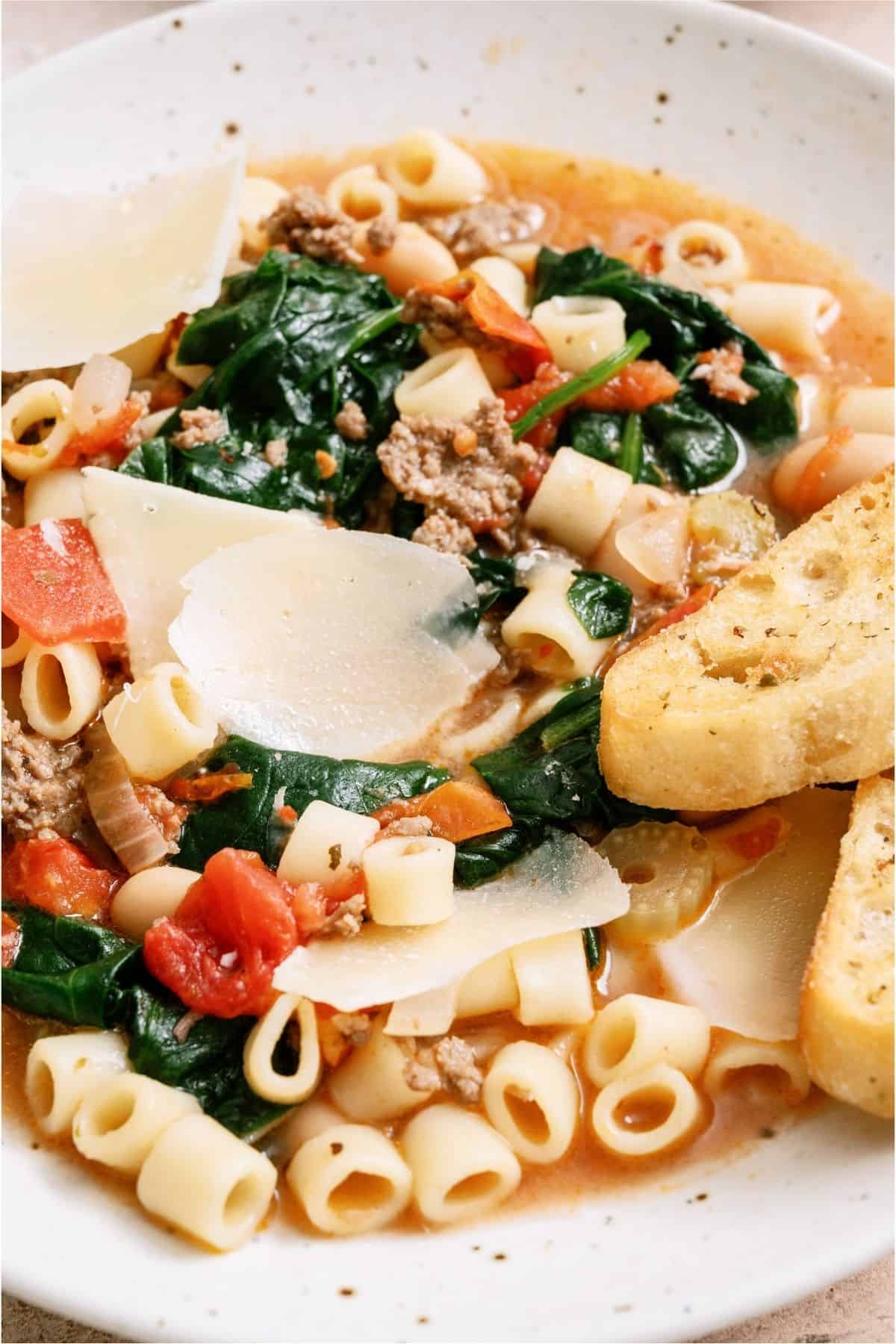 Close up of a bowl of Pasta Fagioli topped with parmesan and a slice of bread.