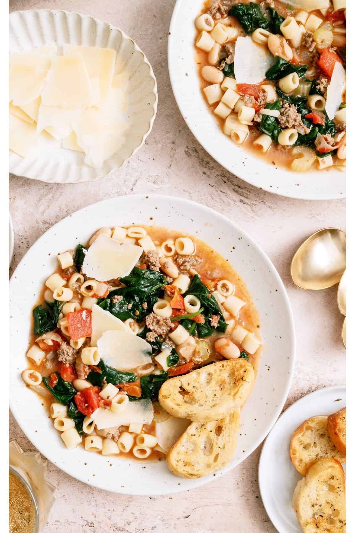Top view of two bowls of Pasta Fagioli with bread and parmesan cheese.