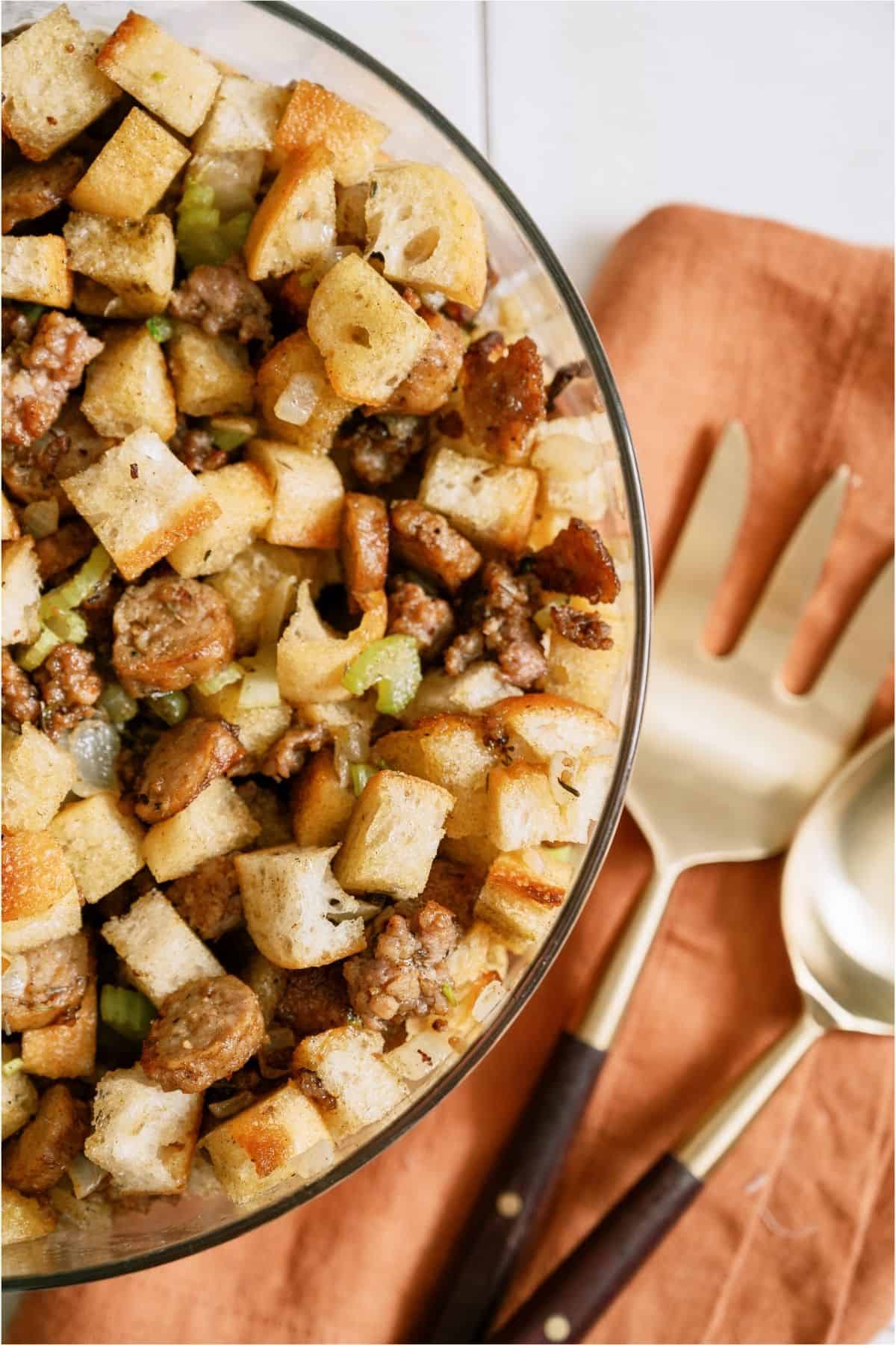 Easy Sausage & Herb Stuffing in a glass bowl with serving utensils on the side.