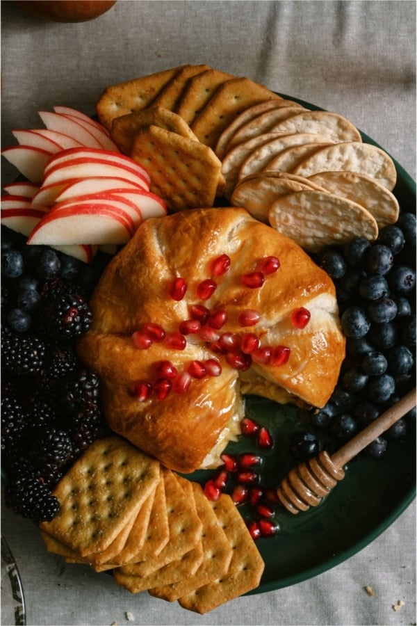 Baked Brie on a plate surrounded by fruit and crackers.