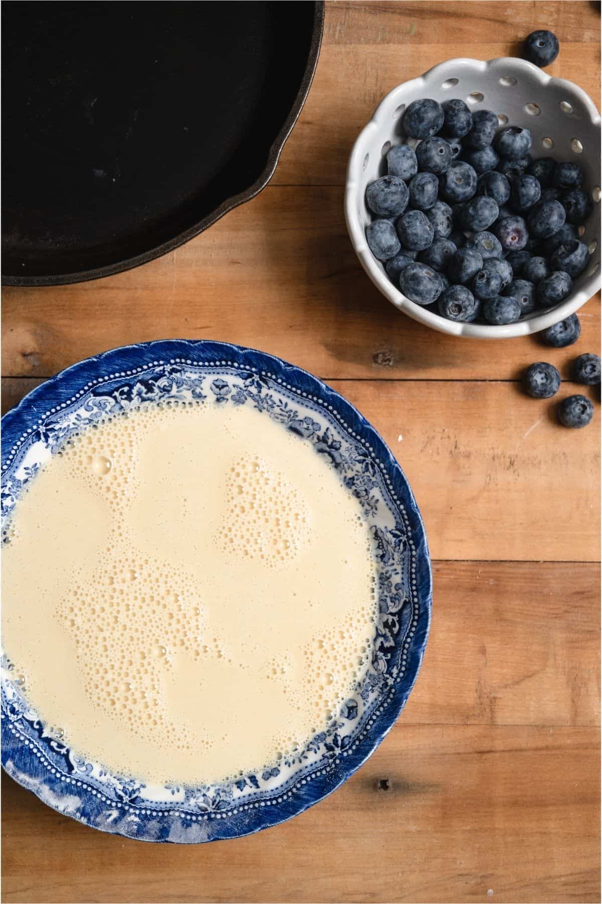 Dutch Baby batter in a bowl with a bowl of fresh blueberries.