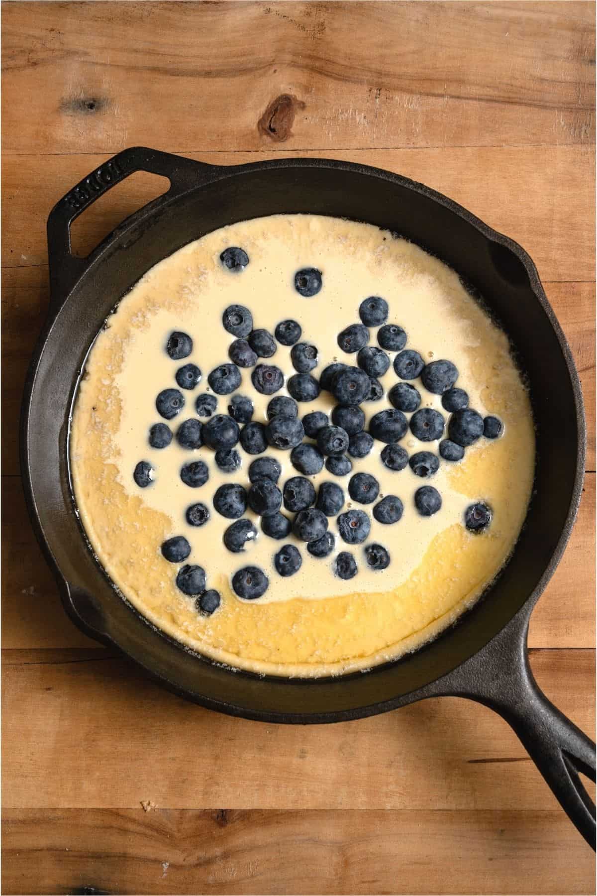 Cast iron skillet filled with  Dutch Baby batter and fresh blueberries.