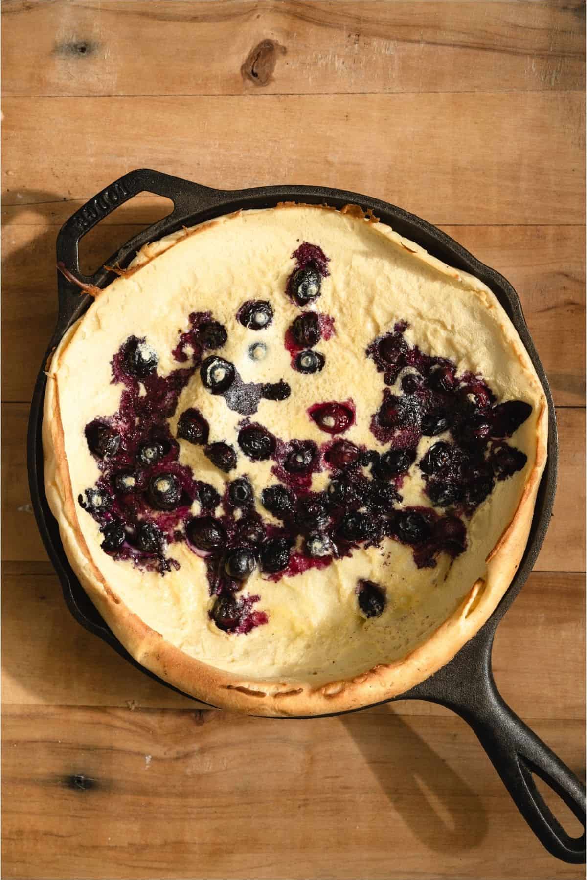 Cooked Dutch Baby with blueberries in cast iron skillet.
