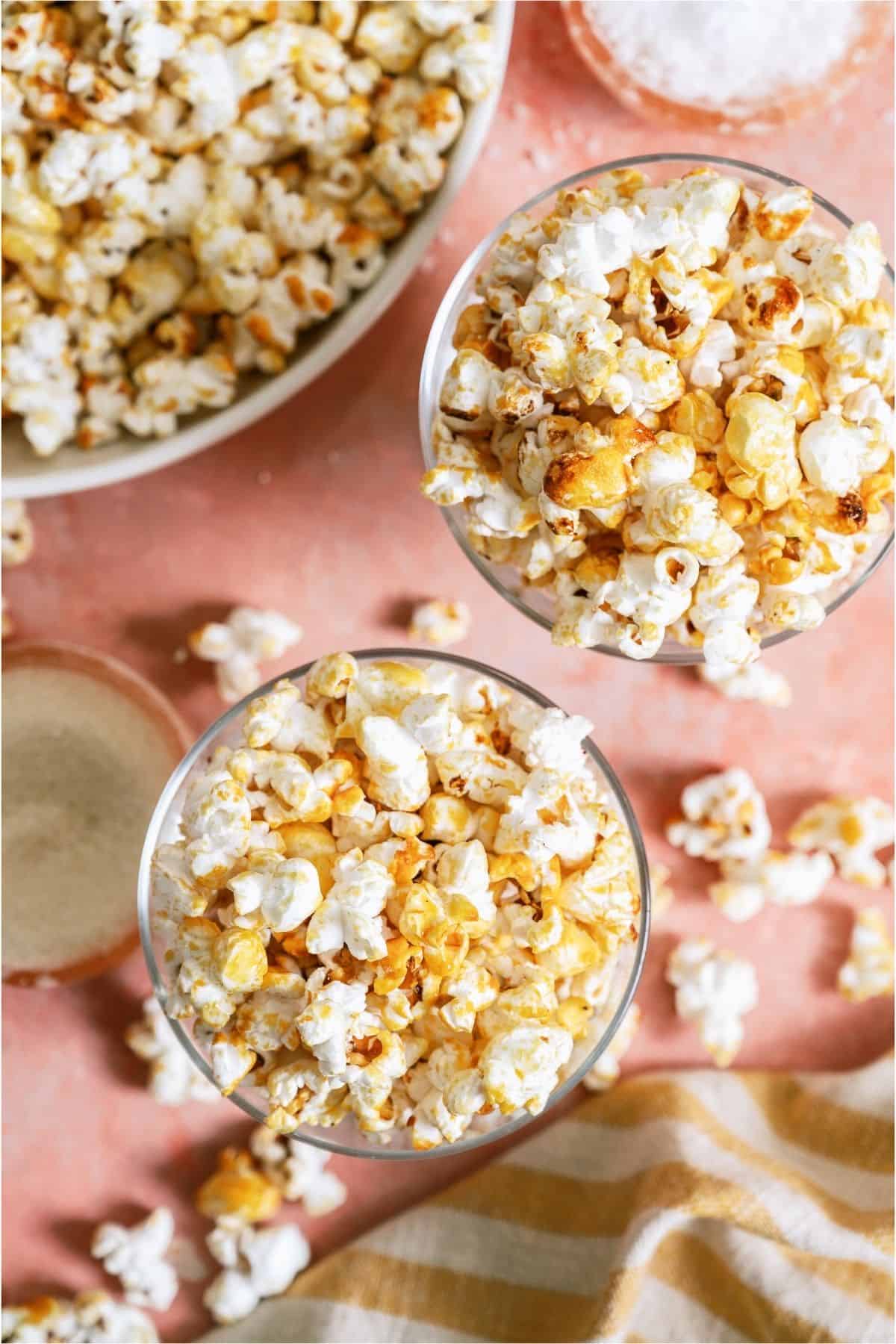 Two glasses filled with Easy Homemade Kettle Corn and a large bowl of Easy Homemade Kettle Corn in the background.