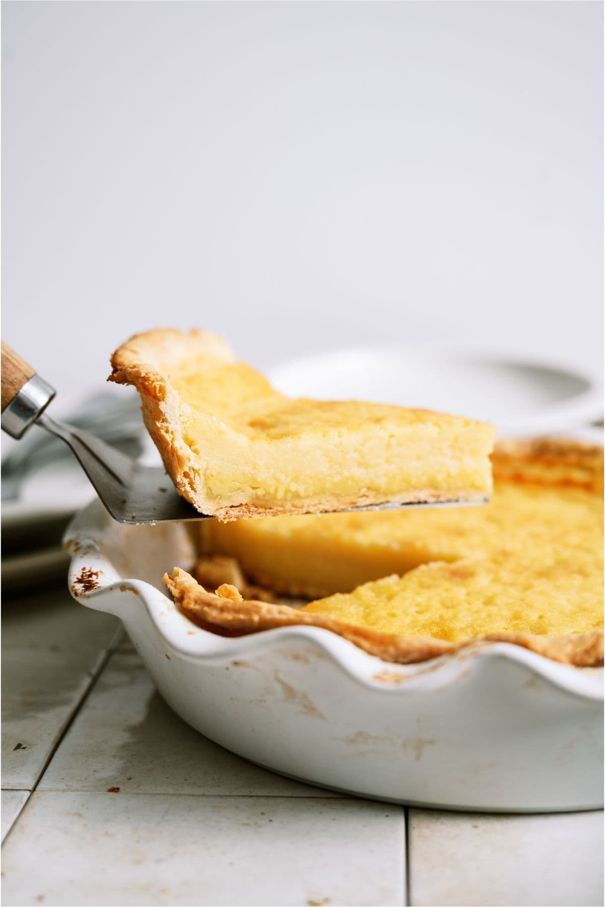 A slice of Homemade Buttermilk Pie being lifted out of a pie plate.