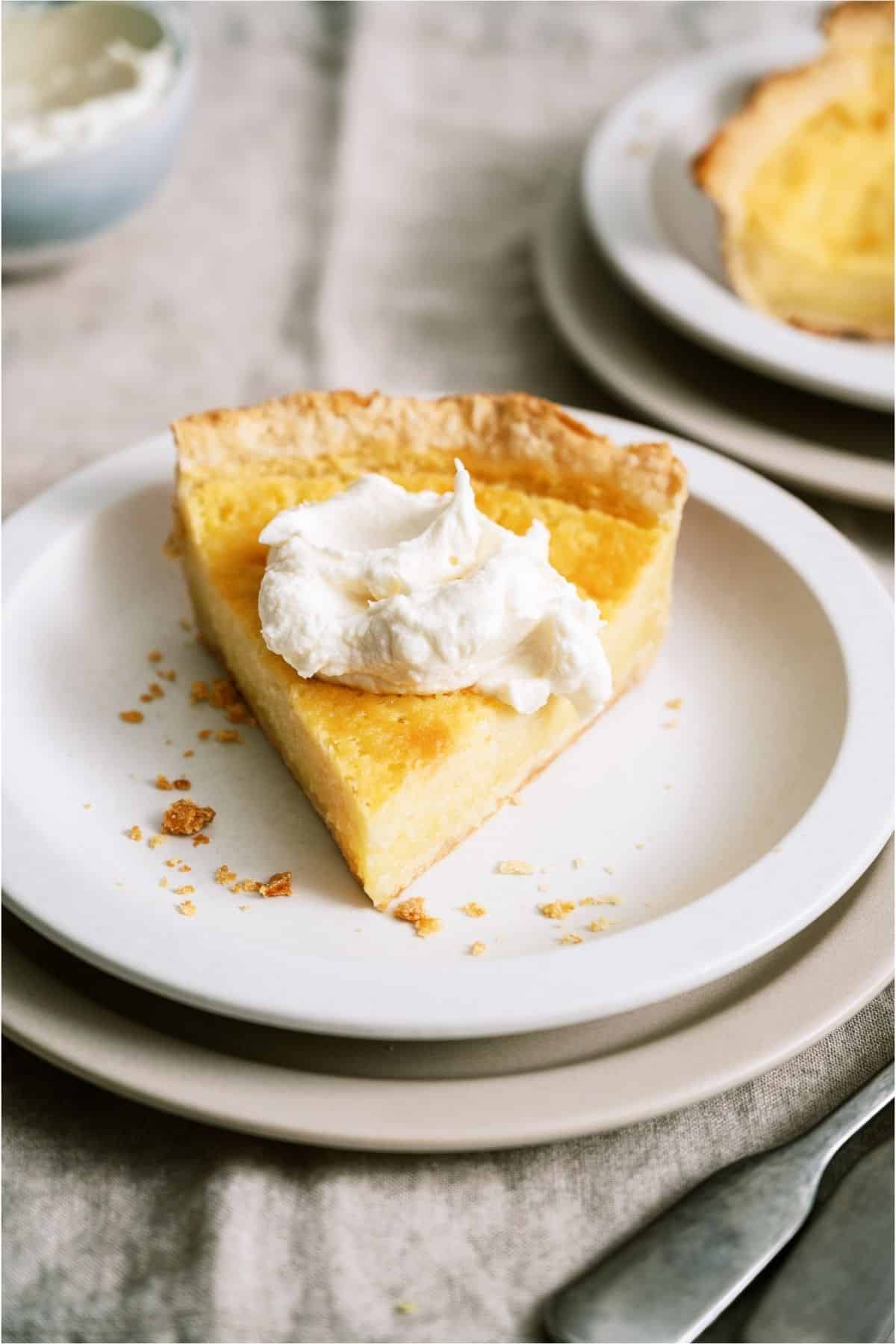 A slice of Homemade Buttermilk Pie on a white plate topped with whip cream.