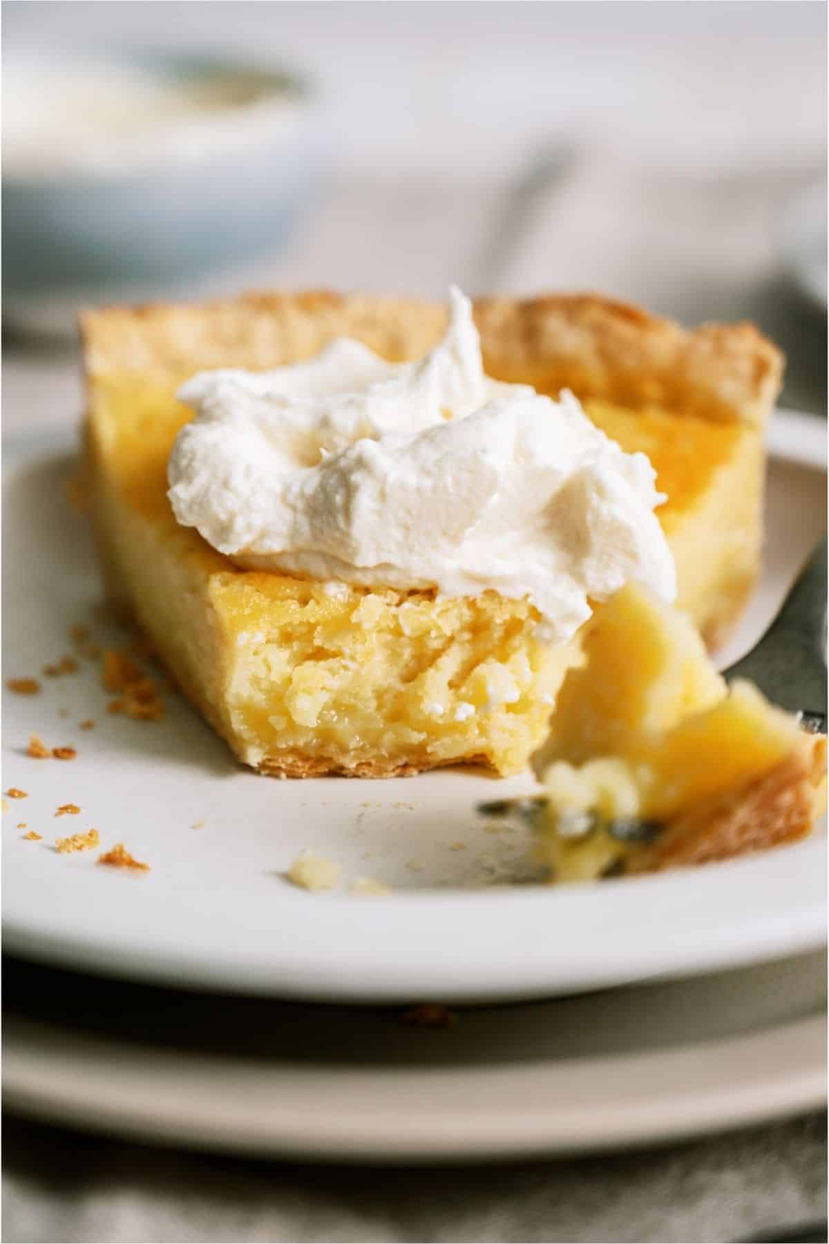 A slice of Homemade Buttermilk Pie on a white plate with a bite missing.