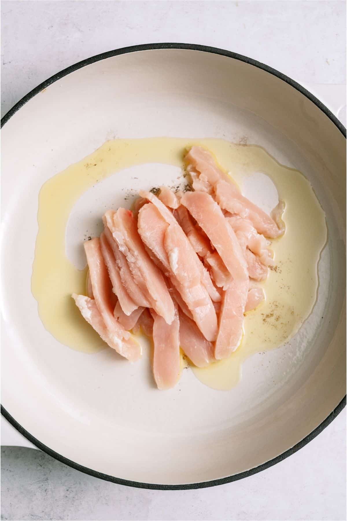 Raw sliced chicken in a skillet.