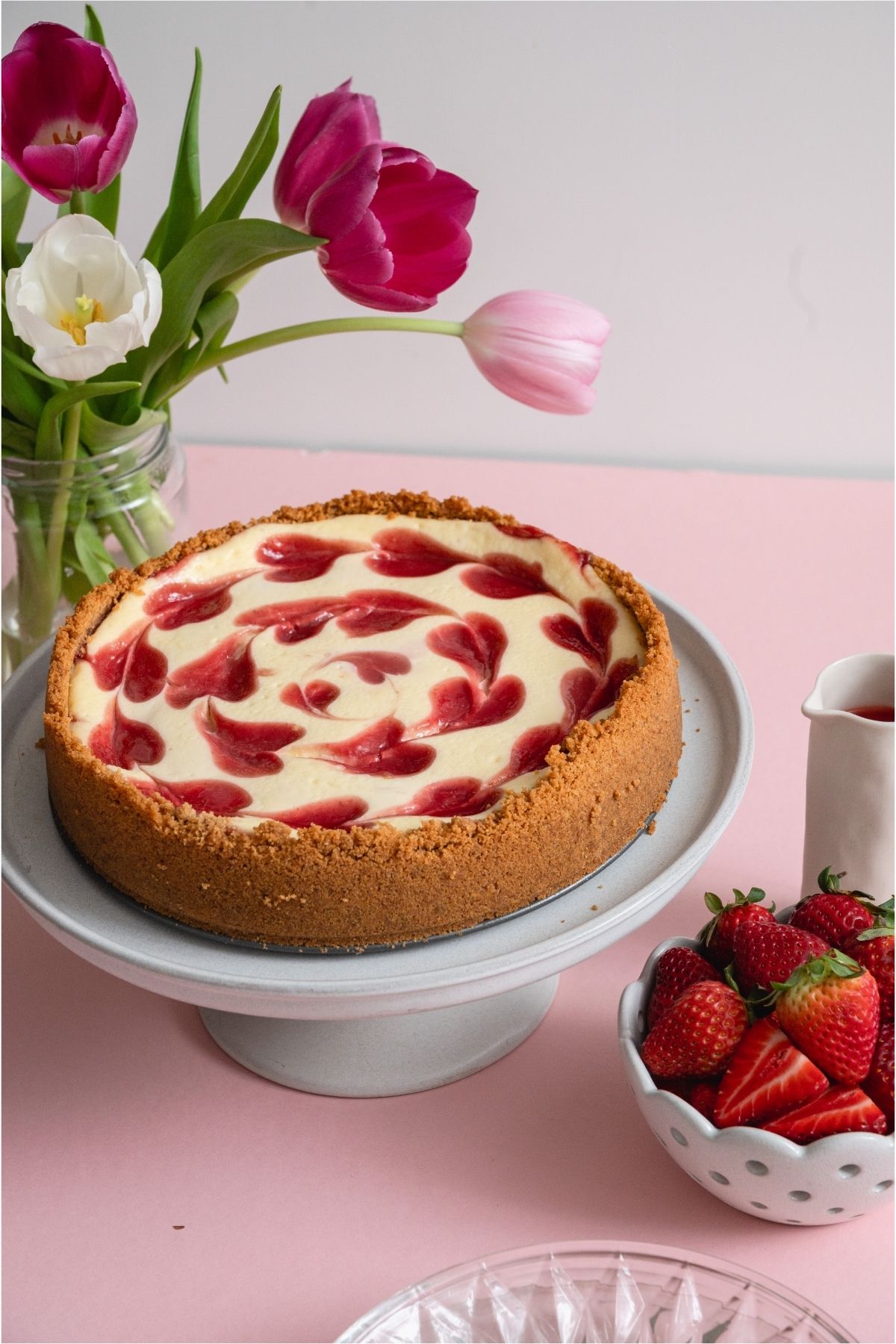 Classic Strawberry Cheesecake on a cake stand next to a bowl of fresh strawberries.