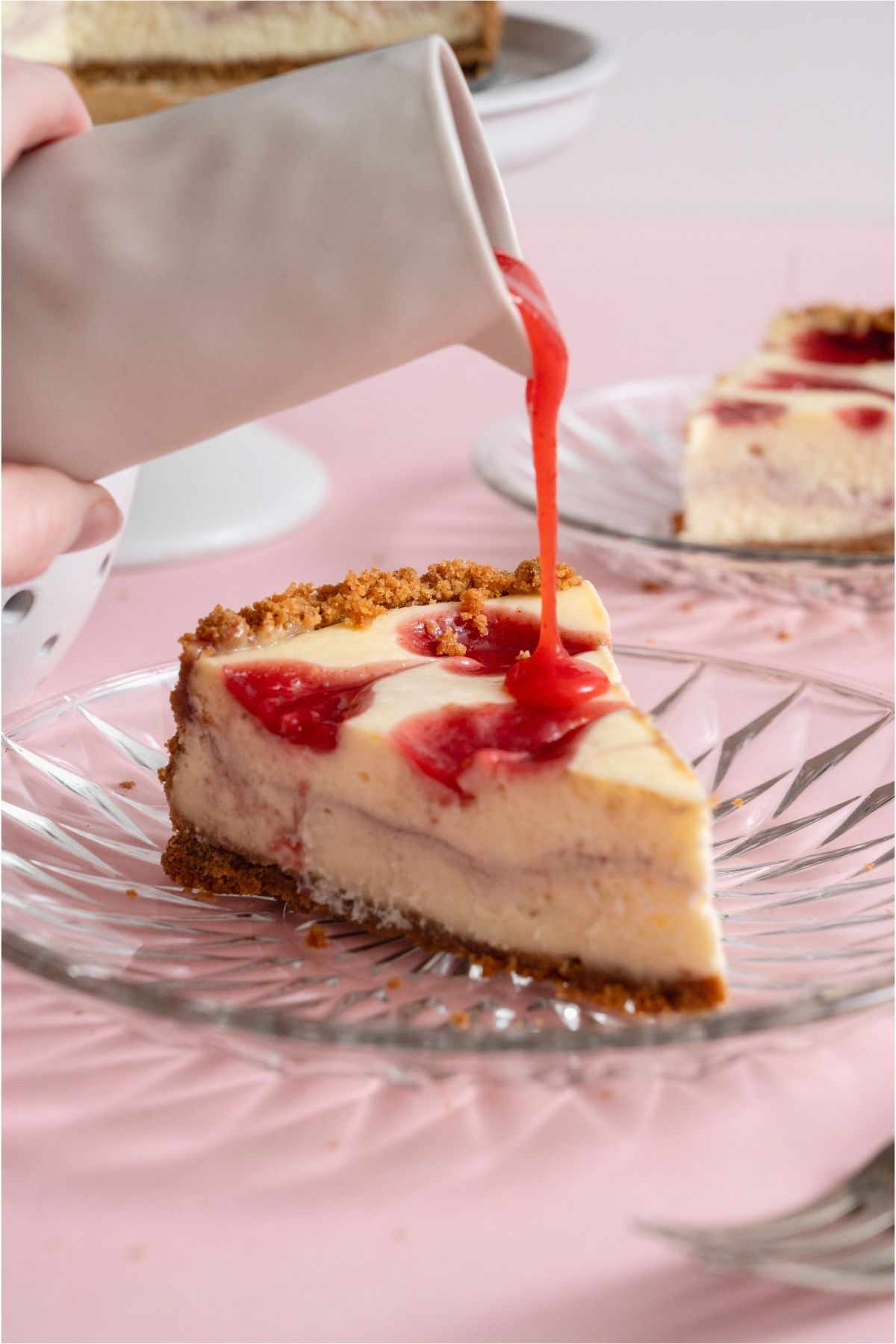 Pouring strawberry sauce on a slice of Classic Strawberry Cheesecake.