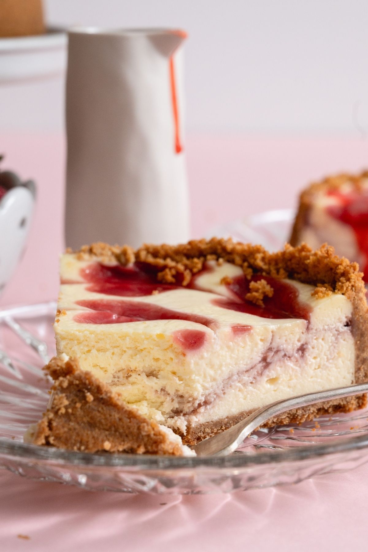 A slice of Classic Strawberry Cheesecake on a plate with a fork slicing a bite.