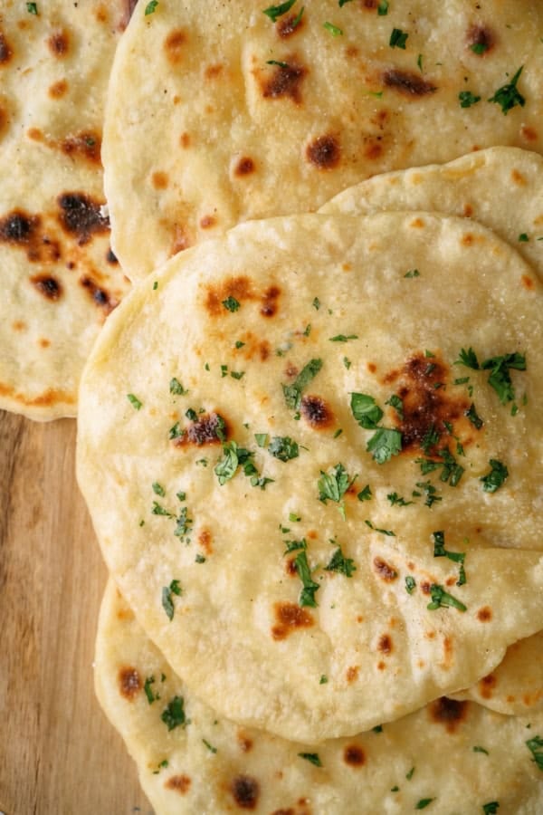 Several pieces of flatbread garnished with chopped herbs are stacked on a wooden surface.