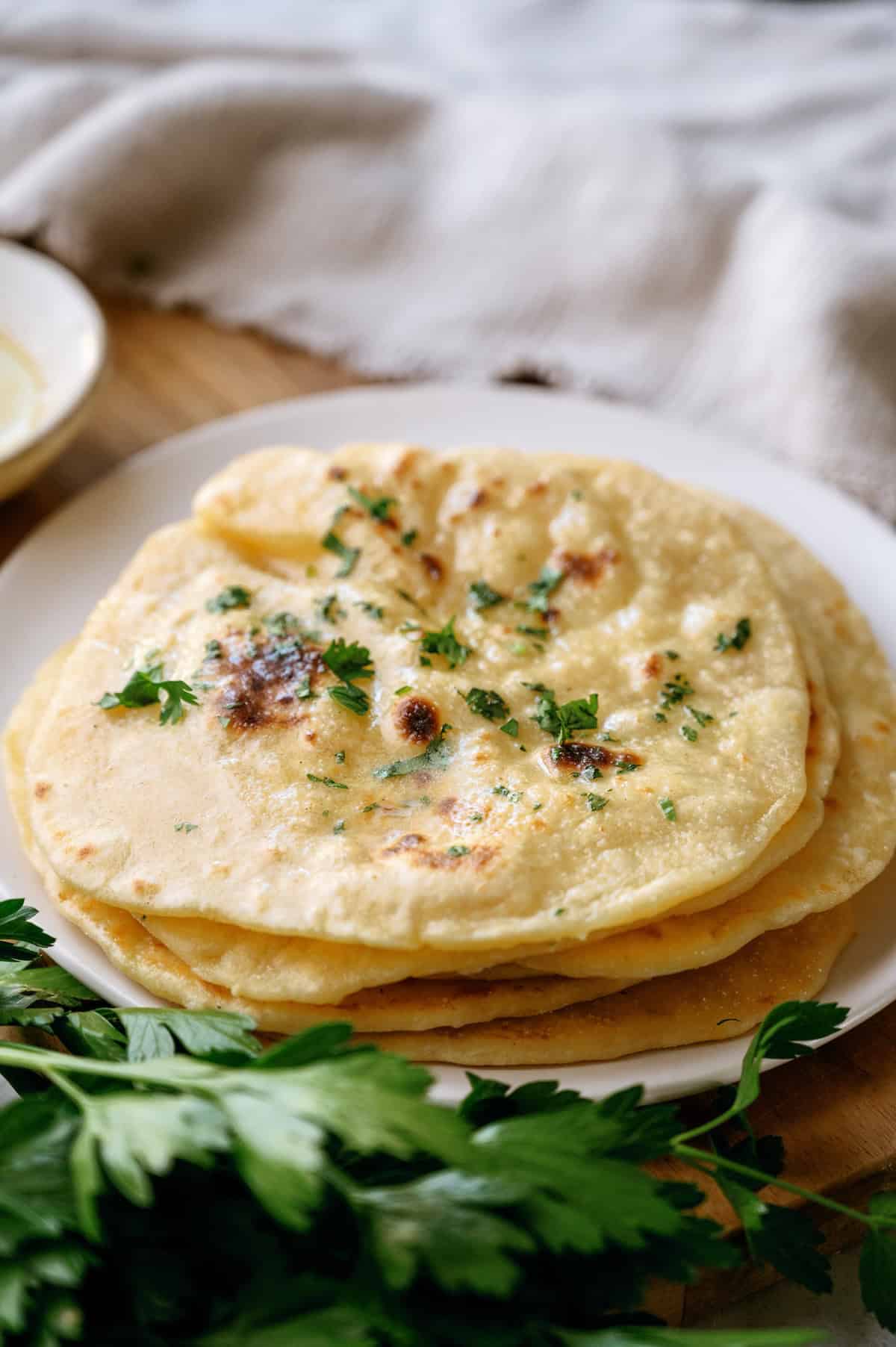 A plate of flatbreads garnished with chopped parsley sits on a wooden surface with fresh parsley nearby.