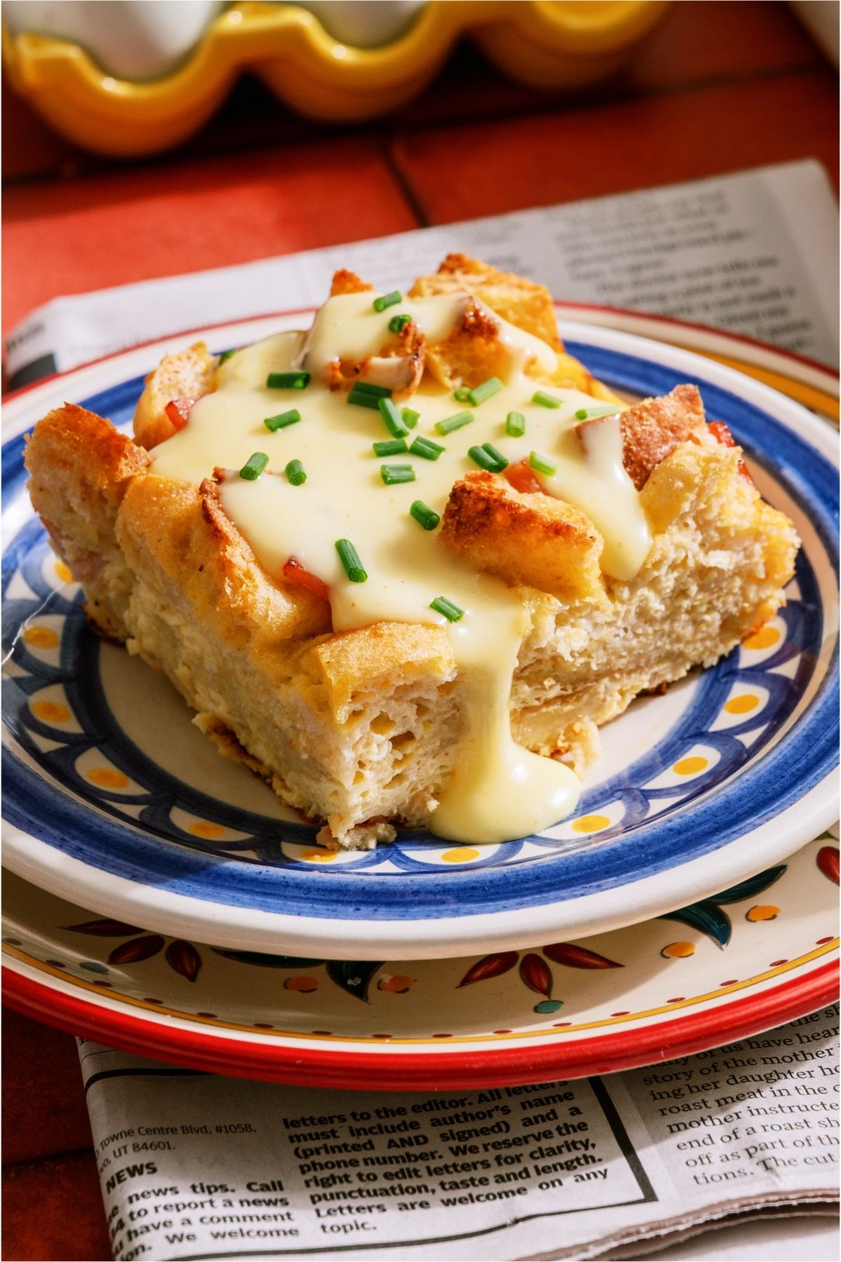 A square of Eggs Benedict Casserole on a plate topped with Hollandaise sauce and chives.